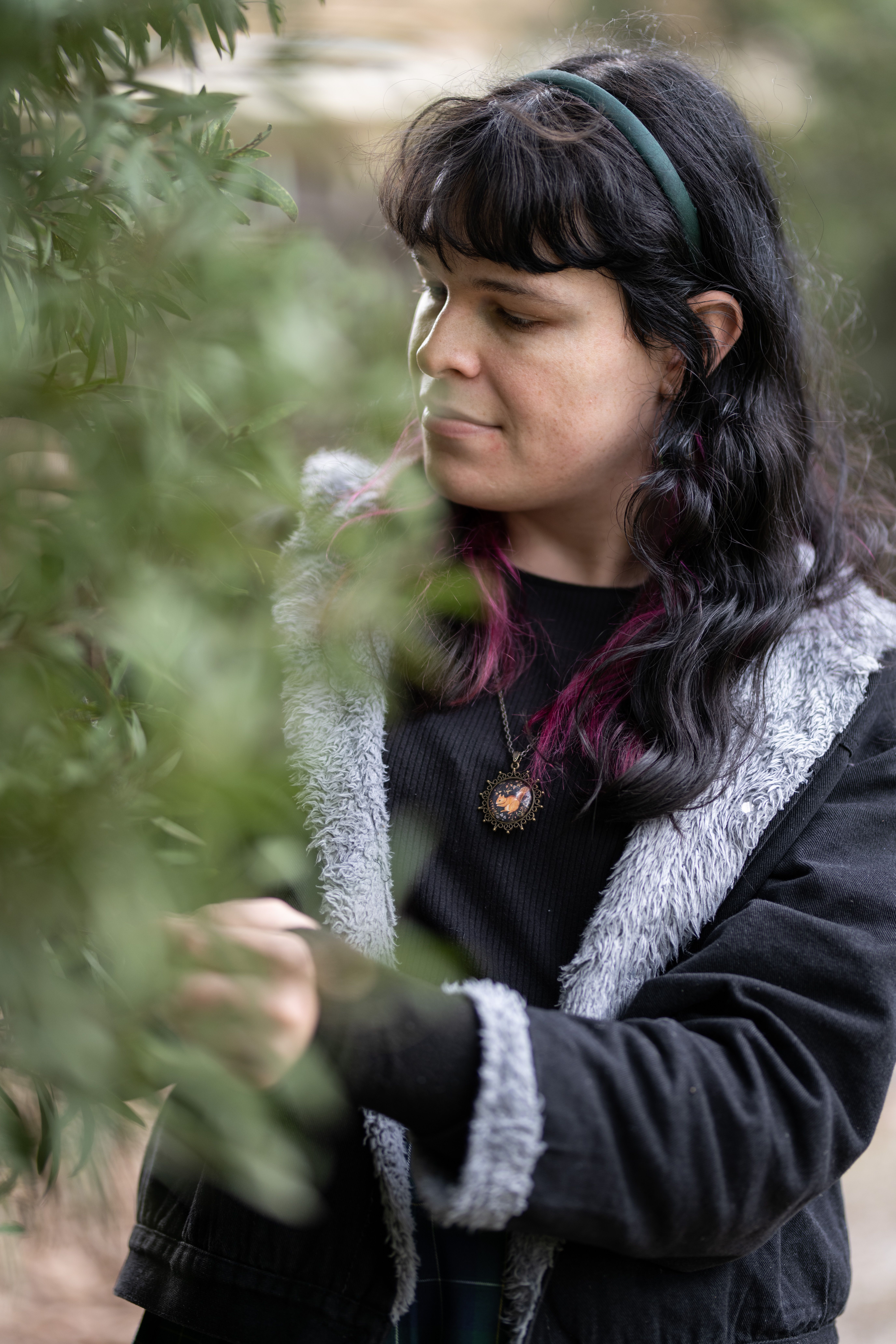 A trans woman in her late 20s pretending to look at some leaves because she's a squirrel