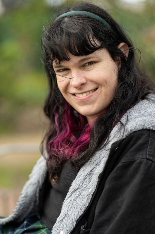 A trans woman in her late 20s smiling at the camera :D